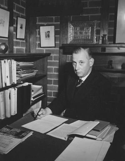 A black and white photo of Maurice Belz sitting at his desk with a pile of papers
