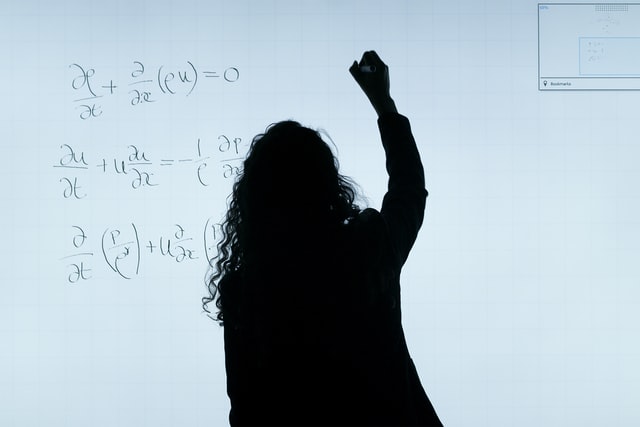 woman in silohuette writing maths equations on a white board